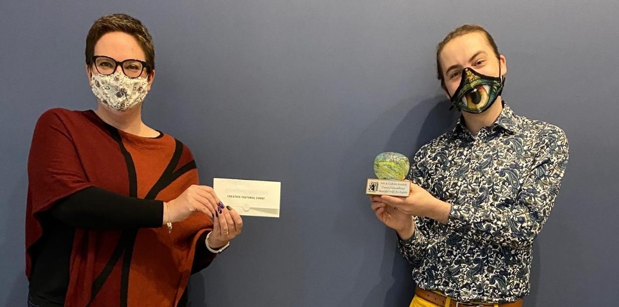 Woman presenting a man with an award.  Both individuals are wearing masks.